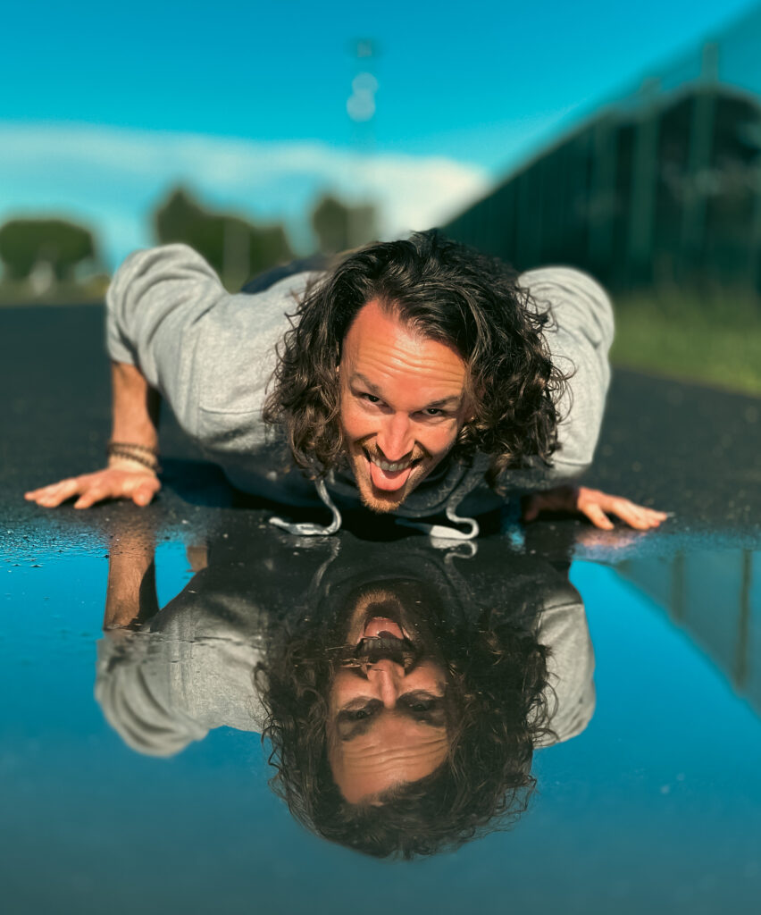 Harold Craston smiling as he leans over a shiny surface that mirrors his face.