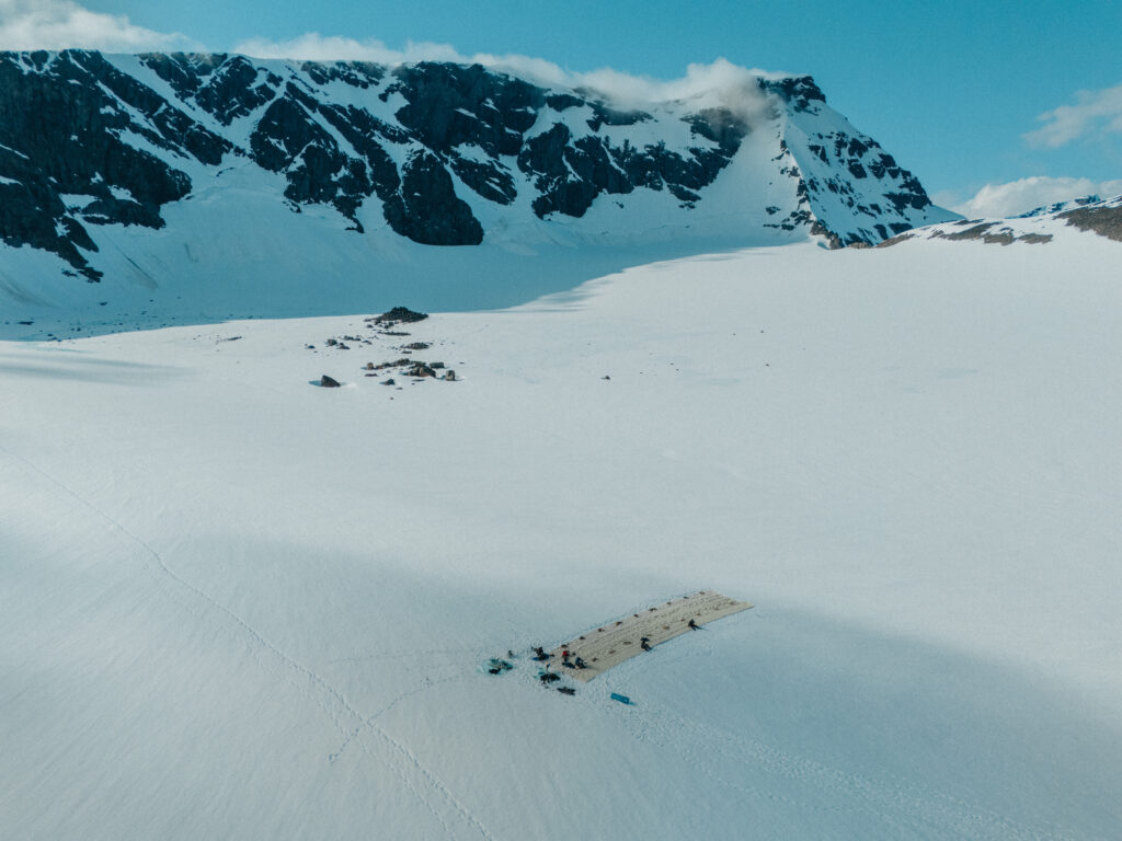 Aerial view of the team rolling out the wool blanket on the snow-covered Björling's glacier, with the mountain ridge behind.