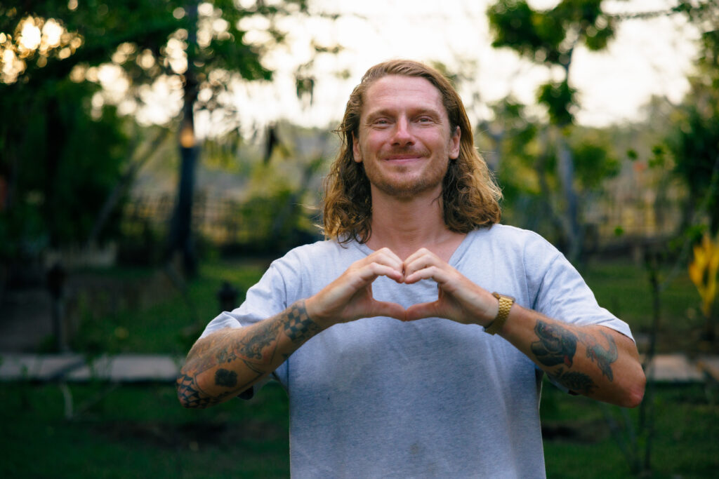 Martin Vrana smiles and makes a heart shape with his hands in a green garden.