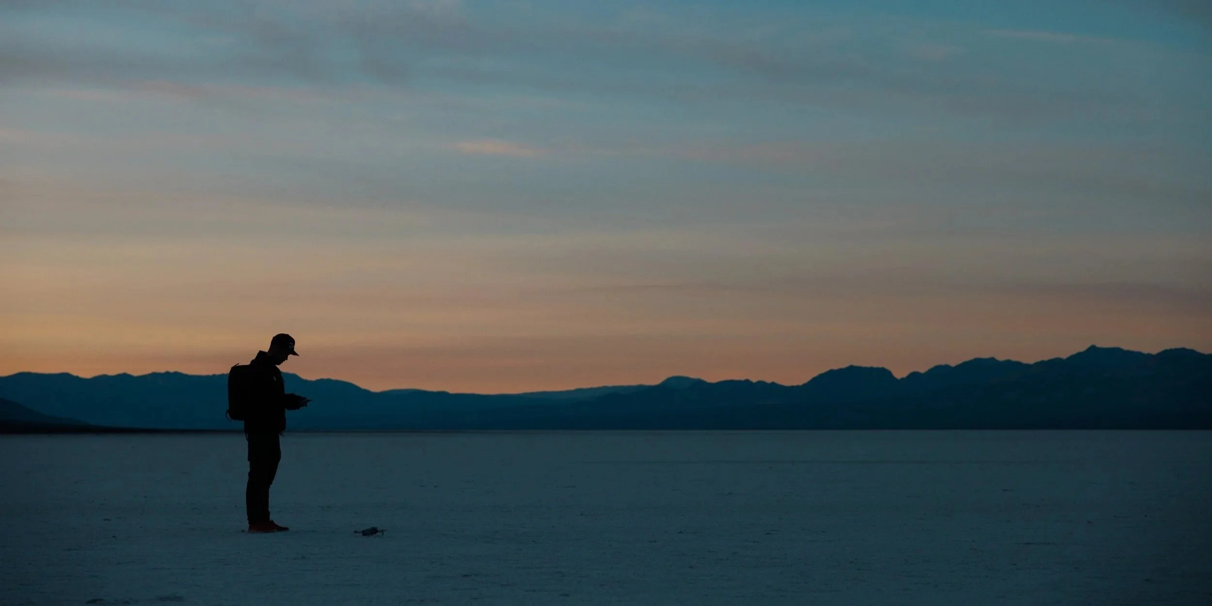 Robin Danehav silhouetted on a wide open plain at dusk, with mountains on the horizon.
