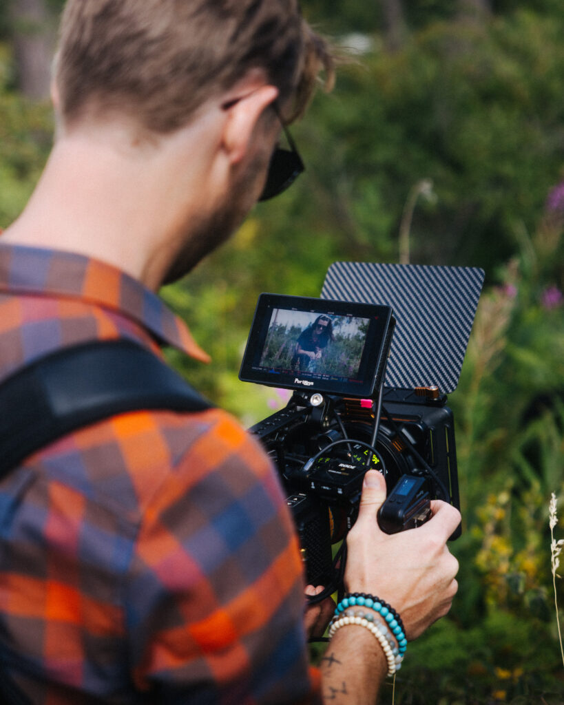 Robin Danehav seen from behind, filming with a RED Komodo camera among green leaves on Gotland.