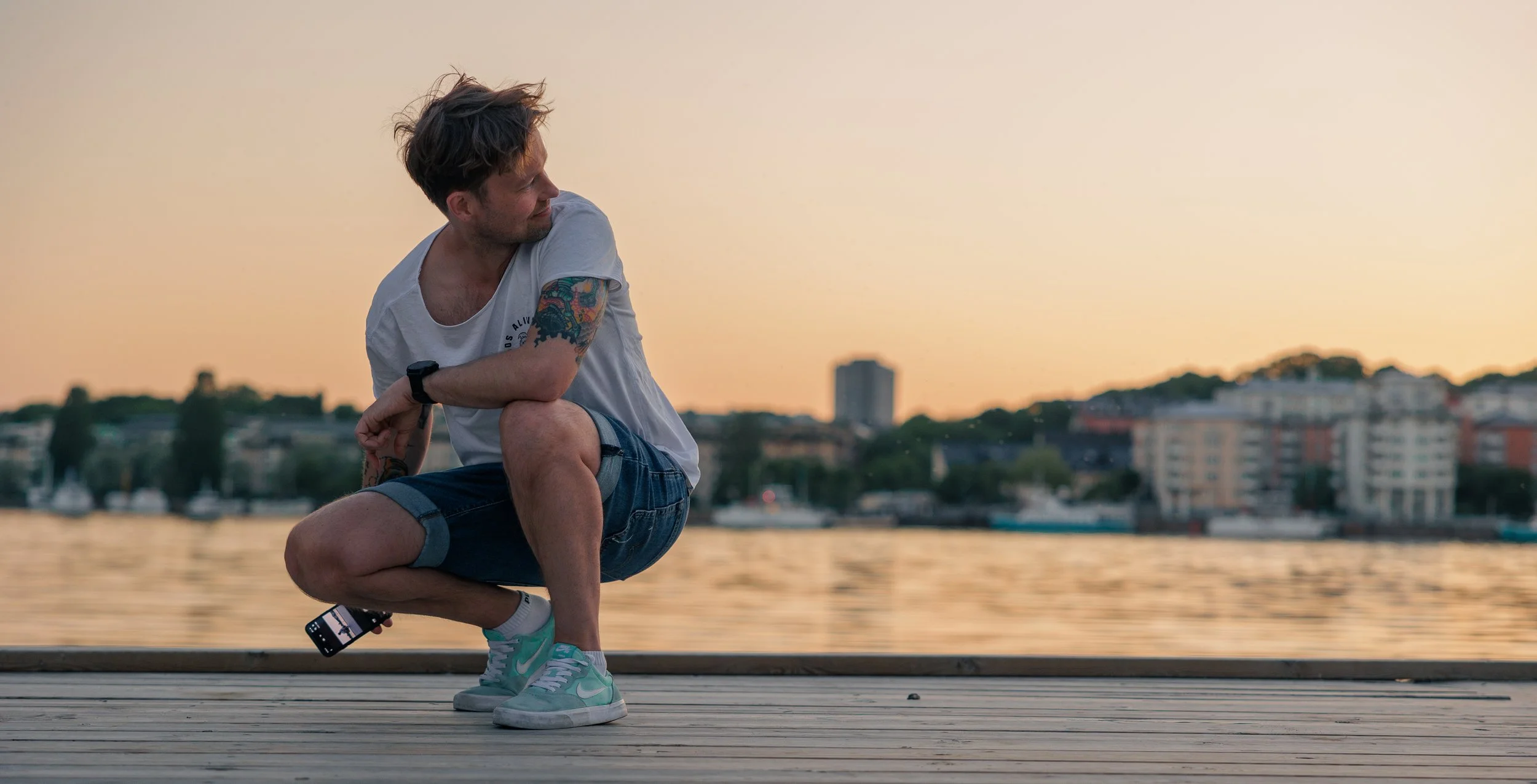 Robin Danehav crouching with a camera by the water at sunset.